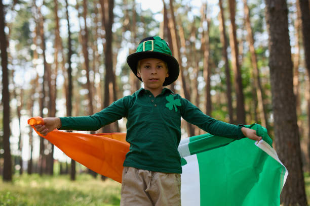 menino leprechaun pequeno celebrando o dia de são patrício com grande bandeira da irlanda nas mãos - republic of ireland flag human face irish culture - fotografias e filmes do acervo