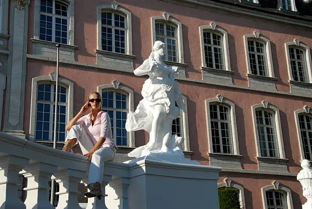 A young beautiful woman takes a phone call in the Palast Garden of Trier the oldest city of Germany.