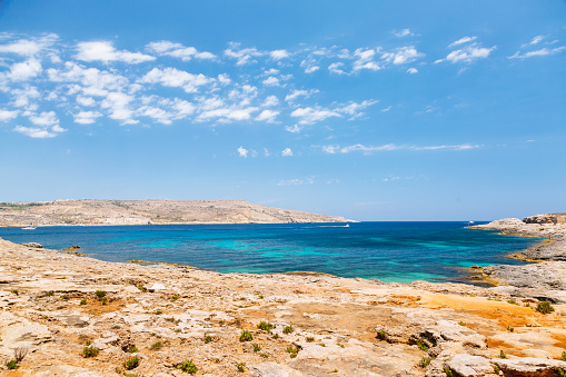 A serene view of the crystal-clear turquoise waters of Comino island (Mediterranean Sea) in Malta. The water is surrounded by rocky cliffs. The sky is blue.
