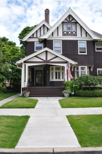 Sidewalk leading to three story tall suburban Victorian style home with American flag