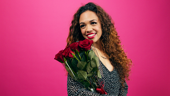 Beautiful multi-ethnic woman holds bunch of red roses, romance, pink studio. High quality photo