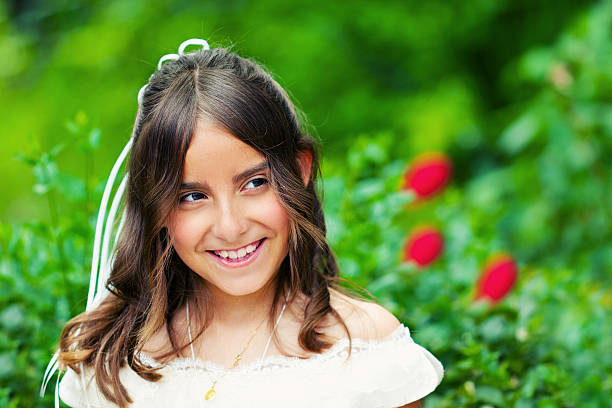 Madrid Spain. May 5, 2018. Close-up shot of young girl looking up pensively wearing communion dress next to sunny tree