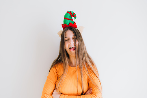 Portrait of beautiful laughing female with long hair, wearing orange top and Elf antlers contemplating Christmas time
