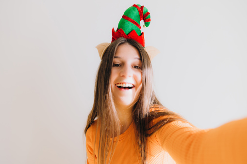 Portrait of beautiful laughing female with long hair, wearing orange top and Elf antlers contemplating Christmas time making photos of herself