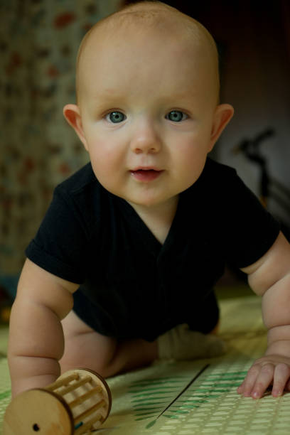 A little boy in a black T-shirt learns to crawl. Close-up portrait of a beautiful baby. Vertical photo