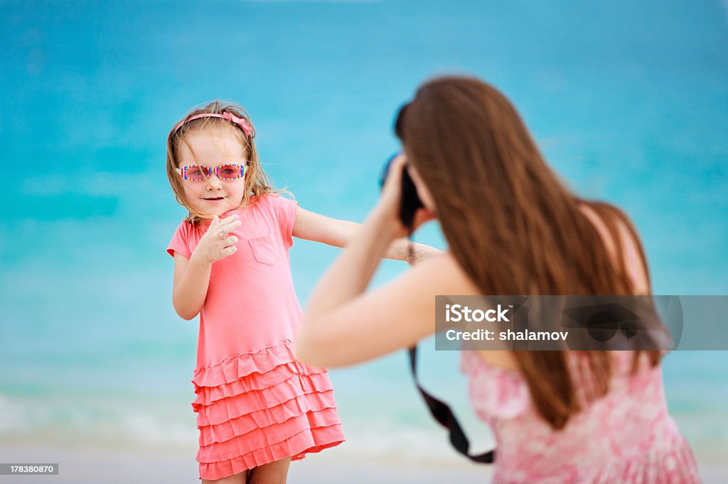 A little girl posing for her mom for a picture at the beach Mother photographing her daughter at tropical beach Adult Stock Photo