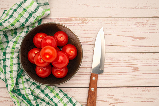Fresh tomatoes on a white plate and a knife with a cloth on a wooden table. Top view. Close-up photo. Health foods concept
