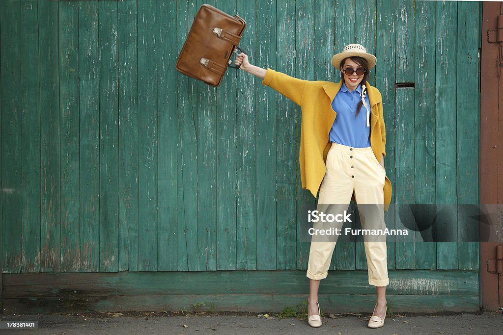 Funny girl Young happy funny (vintage) dressed woman waves retro suitcase. Old green fence on the background. Women Stock Photo