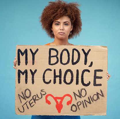 Black woman, portrait and poster to protest abortion, body choice and freedom of human rights in studio. Feminist, rally and sign for safe decision, equality and support of justice on blue background
