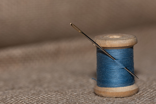 vintage wooden spool with blue threads and needle on a textured light Braun color background.