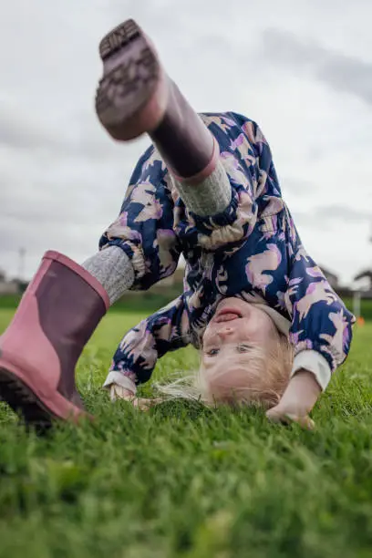 Young girl doing a forward roll while playing outdoors at the park. She is wearing wellies, having fun in the North East of England.