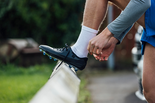 Close up shot of a male football instructor putting on a football boot. He is preparing to coach a football training session on a pitch in the North East of England.