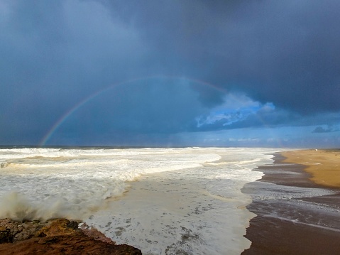 A stunning shot of a rainbow arching over a tranquil ocean, with crests of waves crashing against the shore