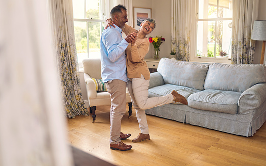 Love, funny and dance with a senior couple in the living room of their home together for bonding. Marriage, retirement or romance with an elderly man and woman laughing in the lounge of their house