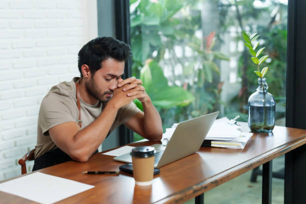 istock Multiethnic male business employee, cafe owner Sitting working in front  tablet doing work documents next  gesture of holding hands thoughtfully disposable paper coffee cup next . Small family cafe 1783869140
