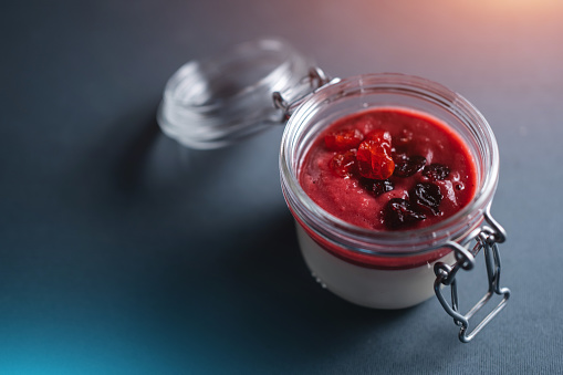 berry panna cotta dessert with cherry sauce in glass jar on black background