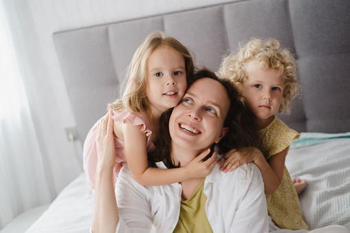 Mother hugging with two little daughters in bed.