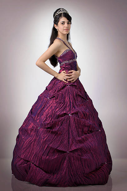 Close-up view of a red dress displayed on a mannequin, featuring a black beaded bow detail at the waist, with soft decorative lights blurred in the background and selective lighting highlighting fabric texture and design.