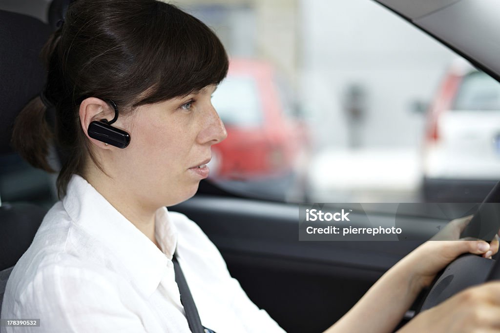 Donna guida, e parlando telefono in auto tramite cuffie - Foto stock royalty-free di Bluetooth