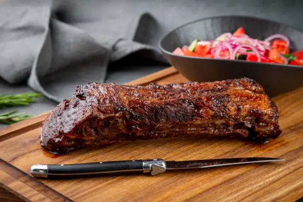 Photo of well-done steak with tomato and cucumber salad on a wooden tray, side view