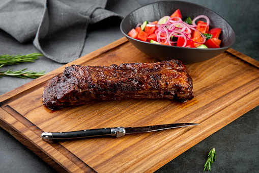 well-done steak with tomato and cucumber salad on a wooden tray, side view