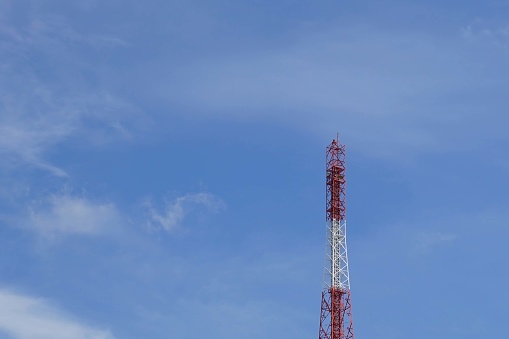 A telecommunication tower with blue sky background, against the blue sky with white clouds.