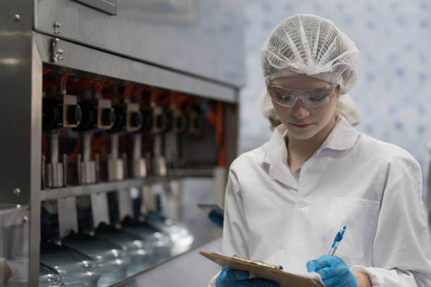 istock Female worker wearing uniform, hairnet working and checking of packaging machine purified drinking plastic bottled water inside automated conveyor belt production line in industry factory 1783922519