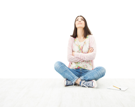 Beautiful girl teenager thinking,  looking up, sitting on floor over white background