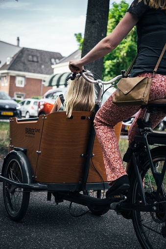 Zeist, Netherlands – August 12, 2022: A mother riding a bicycle, her daughter enjoying the ride in a special wooden compartment