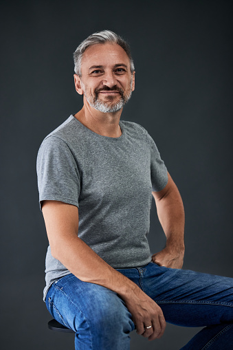 A smiling mature man posing for the camera dressed casually, sitting on a chair.