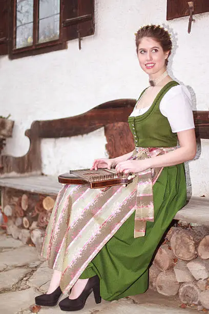 Young Bavarian girl in traditional dress plays music on a zither