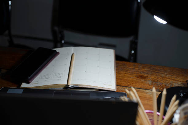 istock Desk for student concept. Laptop for study for exam placed on School table for student work online at home.  Calendar, computer, lamp, and book place on wooden desk at night. 1783938265