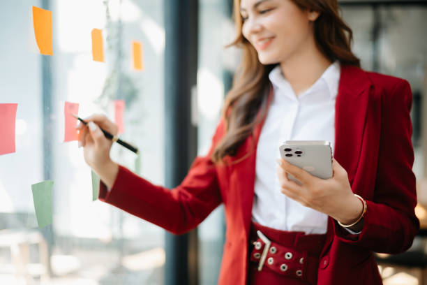 istock Secretary working in modern office in skyscraper, writing and sticking adhesive notes with tasks on window modern office 1783955002