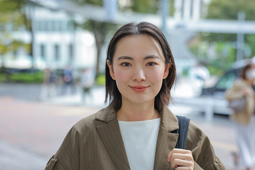 Asian Business Woman looking at camera In Outdoors,  Young woman on her morning commute.
Woman heading to work happily with a cheerful expression on her face.
