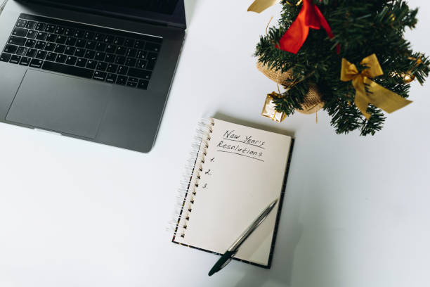 istock open notepad with resolutions for new 2024 year text. Near laptop and christmas tree 1783959420