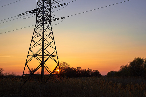 Silhouette of pylon and high voltage power lines against a colorful sky at sunrise or sunset