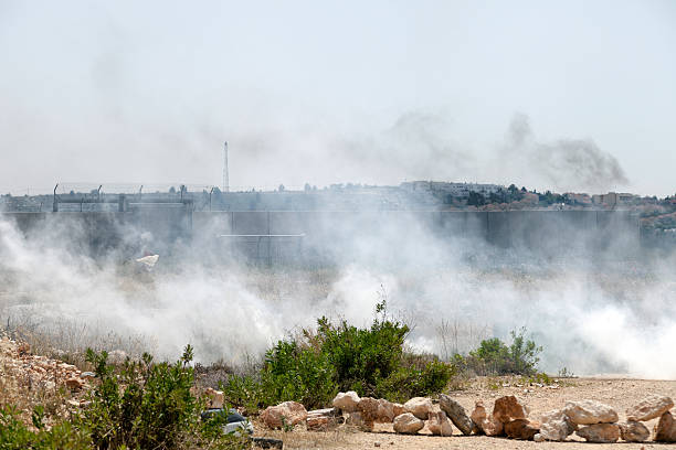 Wall of Separation Palestine Israel Apartheid A cloud of tear gas flying in the wind by the wall of separation between Palestine and Israel, with Israeli soldiers behind the wall. tear gas stock pictures, royalty-free photos & images