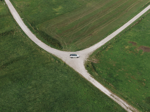 A car in the middle of a crossroad in a rural area as seen from above