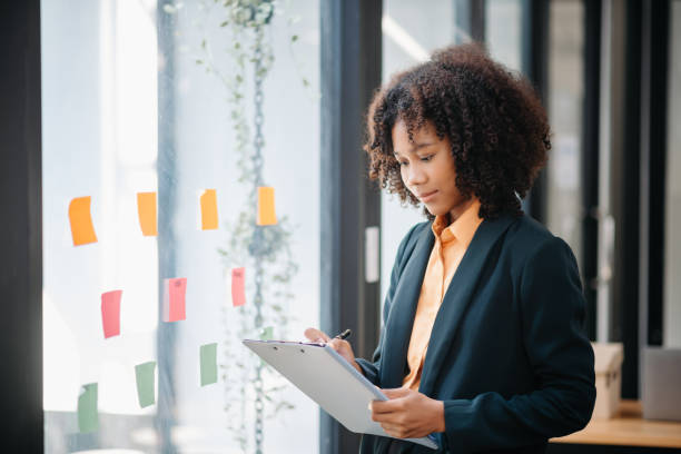 istock Secretary working in modern office in skyscraper, writing and sticking adhesive notes with tasks on window modern office 1783968019