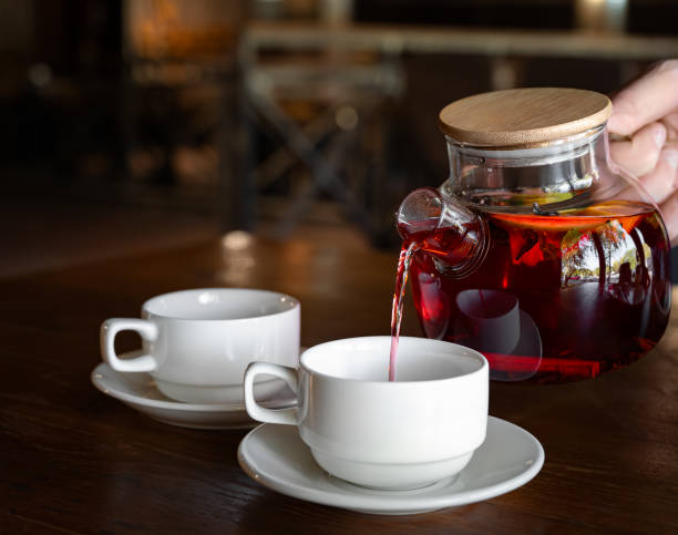 istock A man pours black fragrant fruit tea from a teapot into 2 cups. Tea made from orange, cinnamon, cloves, herbs and sugar. Close-up 1783968581