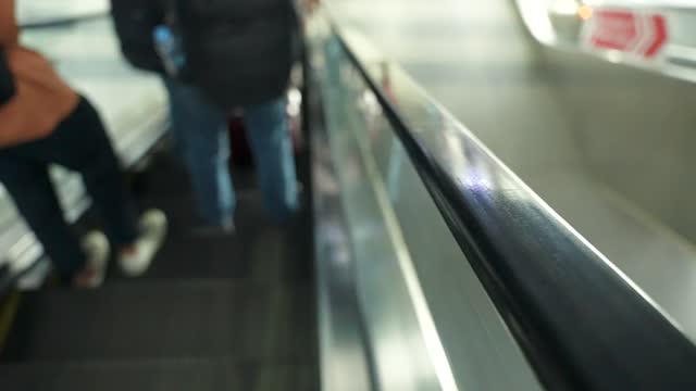 Close up of rubber handrail belt strap of moving down escalator with blurred people in the background.