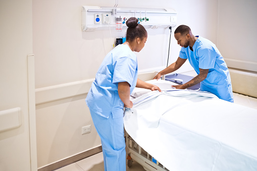 Male and female nurses changing the bed linen on a hospital bed.