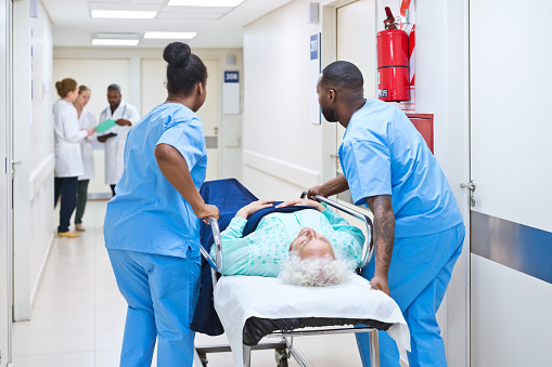 Male and female nurses pushing patient lying on stretcher in hospital.