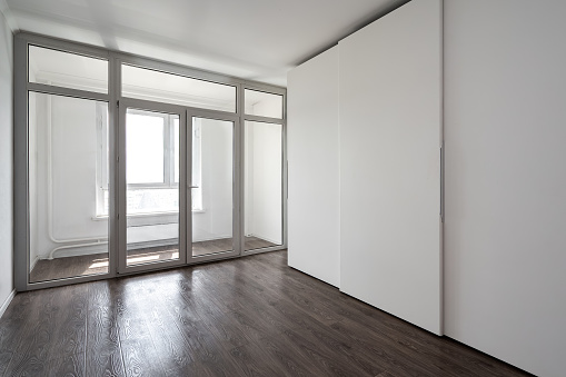 An empty white modern room with a built-in modern wardrobe. Glazed loggia with panoramic windows and a door