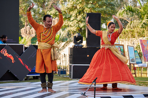 New Delhi, India - 10.12.2022 - Outdoor public park. Indian dancers in ethnic clothing dancing Kathak indian classical dance at outdoor party, couple dancers with small bells Ghungroo on feet performs ancient Kathak dance
