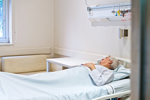 Thoughtful senior man lying on bed in hospital.