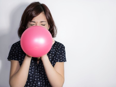 Portrait of a beautiful young woman blowing up a pink balloon on white background