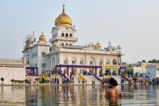 New Delhi, India - 10.11.2022 - Sikh prays in holy pond Sarovar of Gurudwara Bangla Sahib temple in New Delhi, back view of Sikh pilgrim stays in water worships in popular touristic spot in Delhi