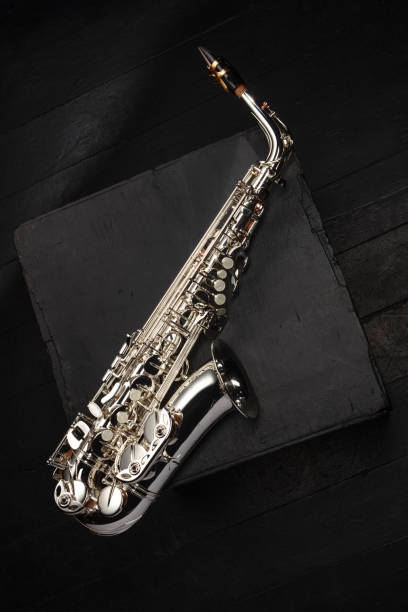 istock Silver saxophone on a worn black cube on a black floor of concert stage 1783982234
