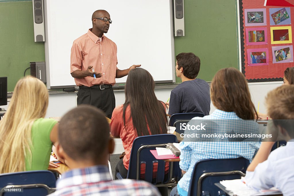 Teacher using interactive whiteboard during class Teacher Using Interactive Whiteboard During Lesson Having A Discussion With Students Teacher Stock Photo